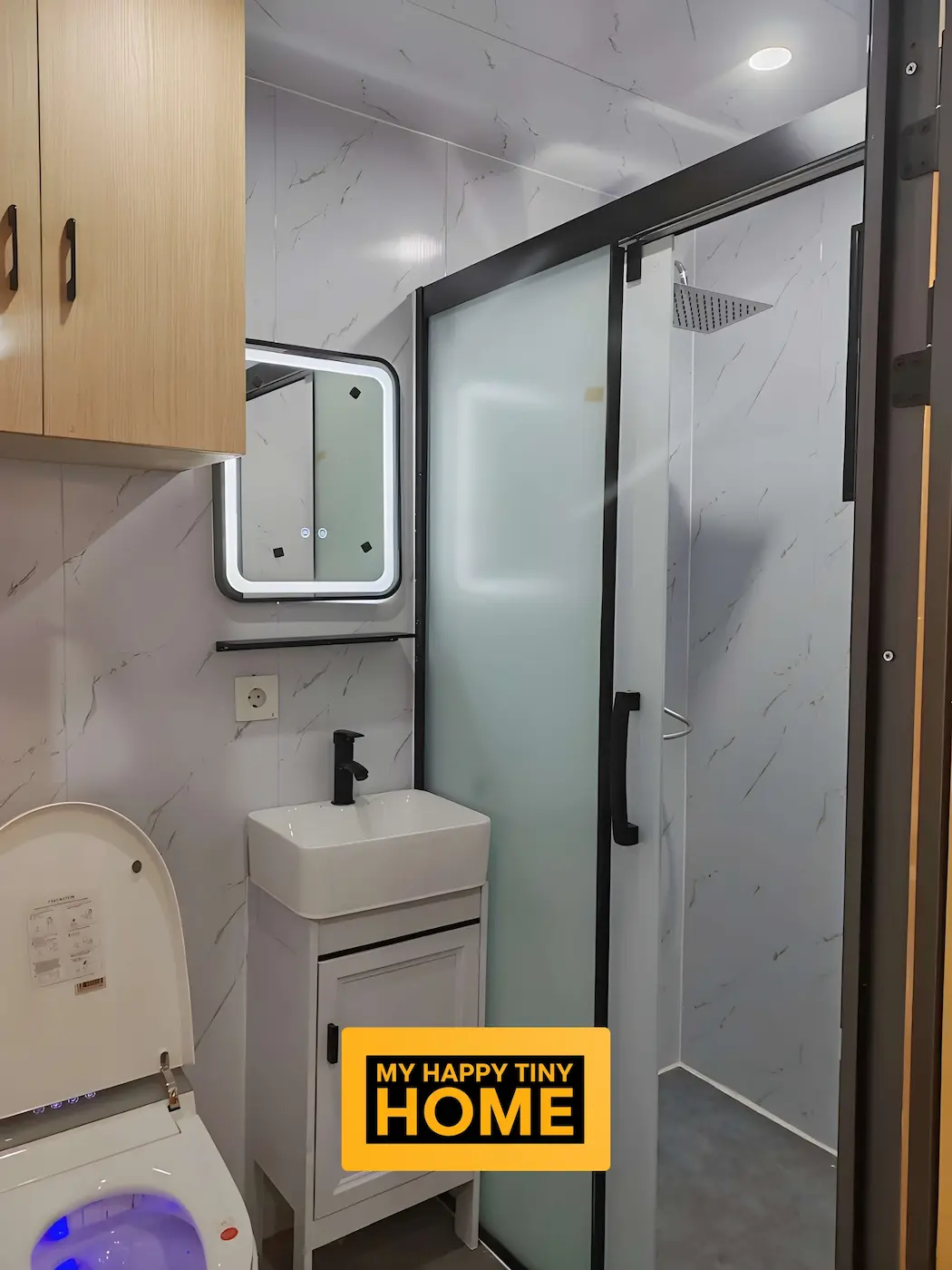 Bathroom interior of a prefab pod featuring vanity, mirror, toilet and full-width shower